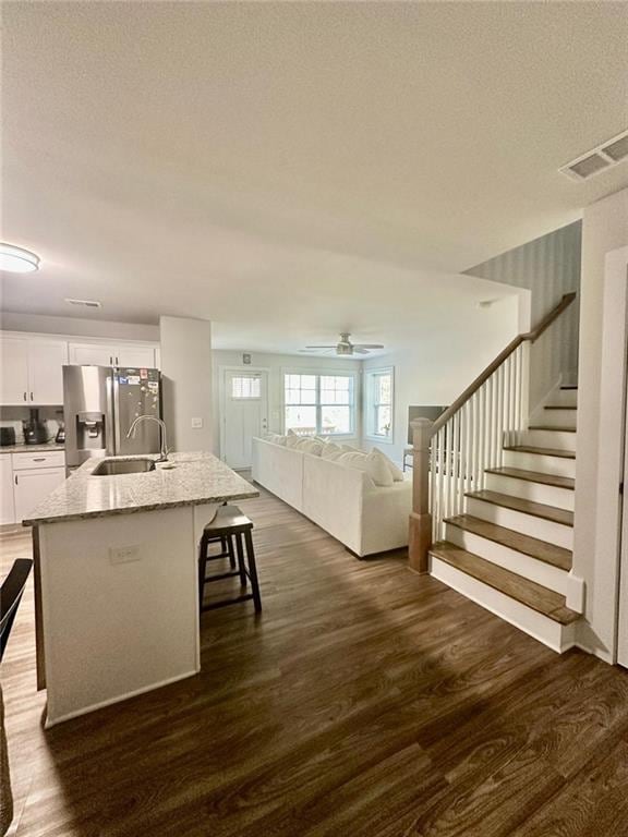 kitchen with stainless steel refrigerator with ice dispenser, a kitchen bar, an island with sink, white cabinets, and light stone counters