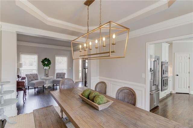 dining space featuring wainscoting, a raised ceiling, dark wood-type flooring, and ornamental molding