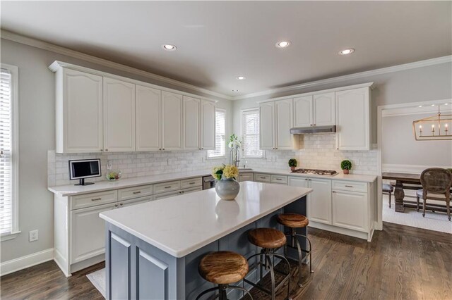 kitchen with white cabinets, ornamental molding, under cabinet range hood, and stainless steel gas cooktop