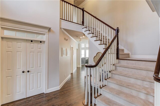 staircase featuring crown molding, a high ceiling, wood finished floors, and baseboards