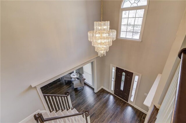 entrance foyer featuring baseboards, stairway, wood finished floors, a towering ceiling, and an inviting chandelier