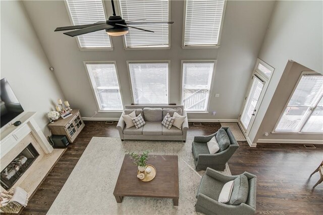 living area featuring visible vents, a ceiling fan, wood finished floors, baseboards, and a towering ceiling