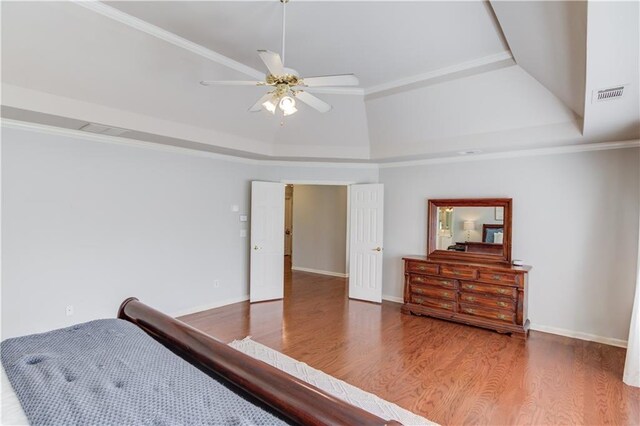 bedroom featuring visible vents, ornamental molding, a tray ceiling, wood finished floors, and baseboards