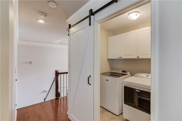 laundry room with light wood-type flooring, washer and dryer, a barn door, cabinet space, and crown molding