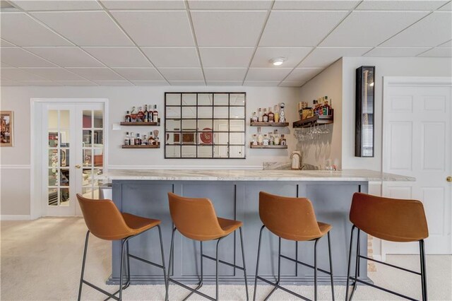 bar featuring a dry bar, light colored carpet, french doors, and a paneled ceiling