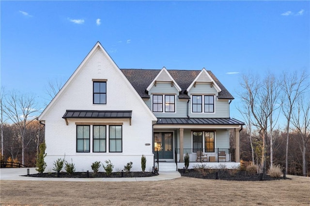 modern inspired farmhouse featuring metal roof, covered porch, brick siding, a front lawn, and a standing seam roof