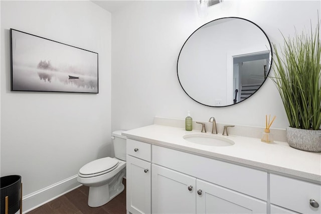 half bathroom featuring toilet, wood finished floors, vanity, and baseboards