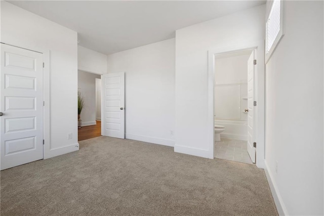 unfurnished bedroom with carpet floors, baseboards, and ensuite bathroom