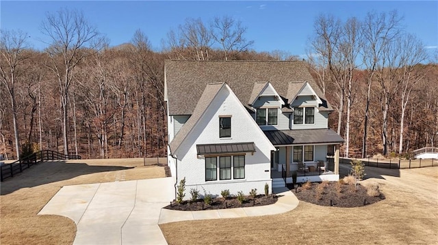 view of front of home with metal roof, a porch, fence, driveway, and a standing seam roof