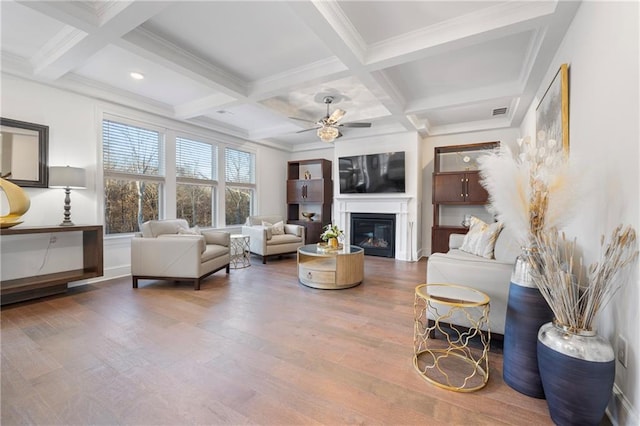 living room featuring coffered ceiling, a ceiling fan, a glass covered fireplace, wood finished floors, and beam ceiling