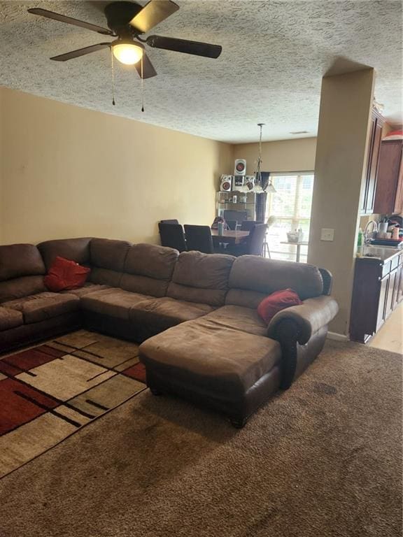 carpeted living room with a textured ceiling, ceiling fan with notable chandelier, and sink