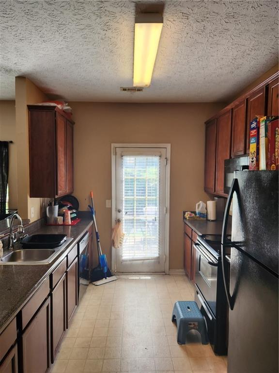 kitchen with light tile floors, a textured ceiling, black appliances, and sink