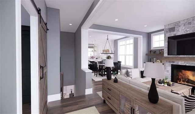 bedroom featuring a barn door, dark hardwood / wood-style flooring, a stone fireplace, and a notable chandelier