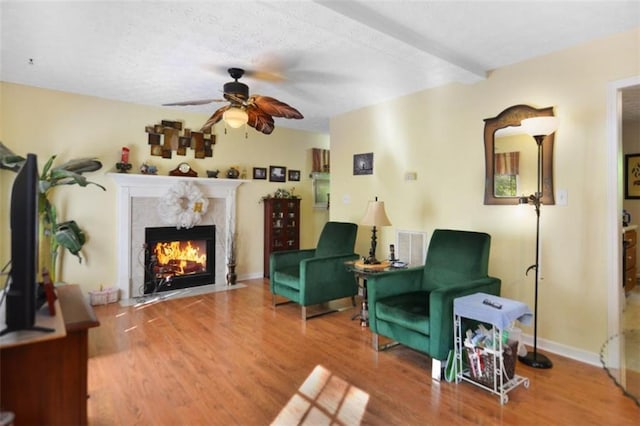 living area featuring beamed ceiling, ceiling fan, and wood-type flooring