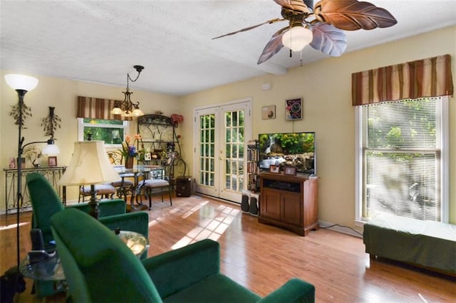 living room with ceiling fan with notable chandelier, light hardwood / wood-style floors, french doors, and a textured ceiling