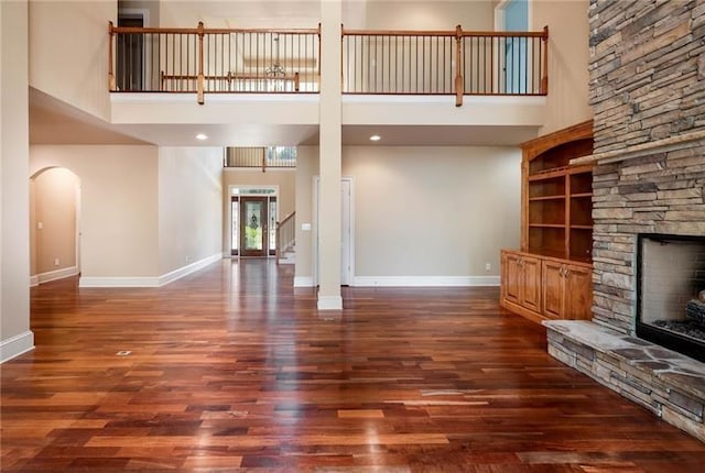 unfurnished living room with a high ceiling, a stone fireplace, and dark wood-type flooring