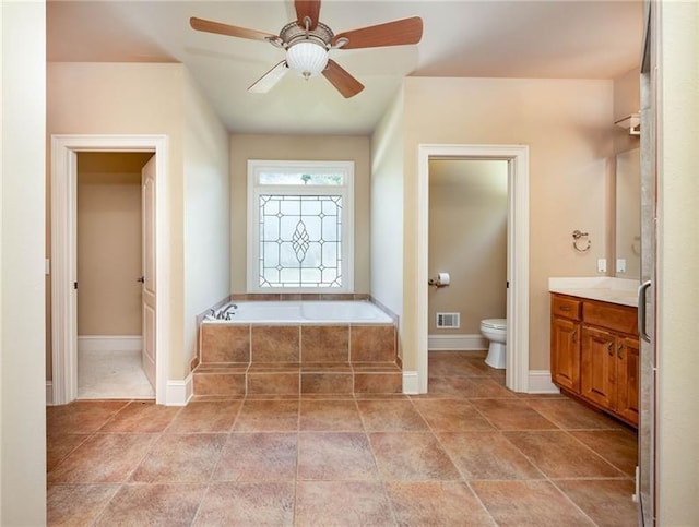 bathroom with vanity, tiled tub, toilet, and ceiling fan