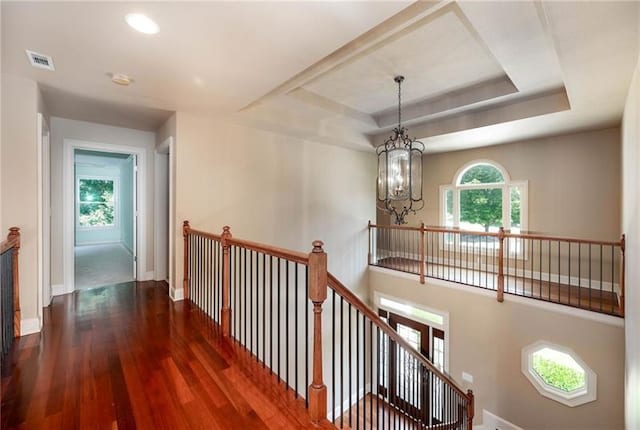 hallway featuring a notable chandelier, dark wood-type flooring, and a raised ceiling