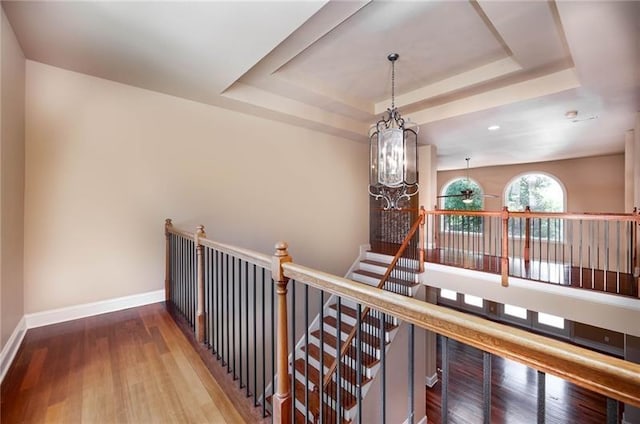 corridor featuring a chandelier, a raised ceiling, and hardwood / wood-style floors