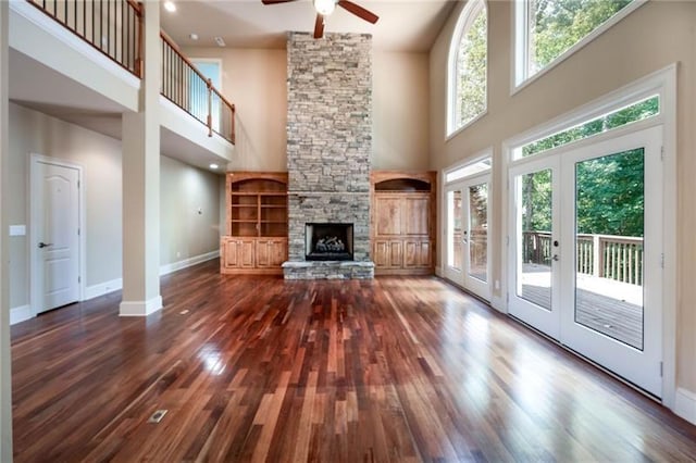 unfurnished living room with french doors, dark hardwood / wood-style floors, a towering ceiling, ceiling fan, and a fireplace