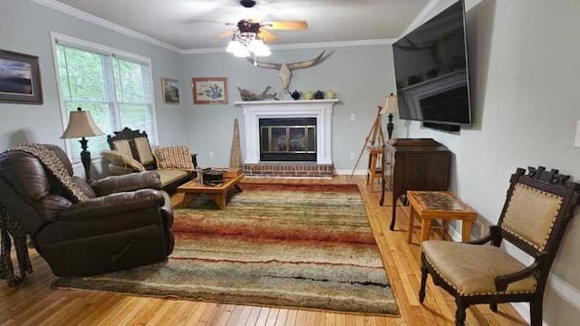 living area with hardwood / wood-style flooring, a brick fireplace, ceiling fan, ornamental molding, and baseboards