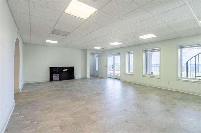 unfurnished living room featuring arched walkways, baseboards, and a drop ceiling