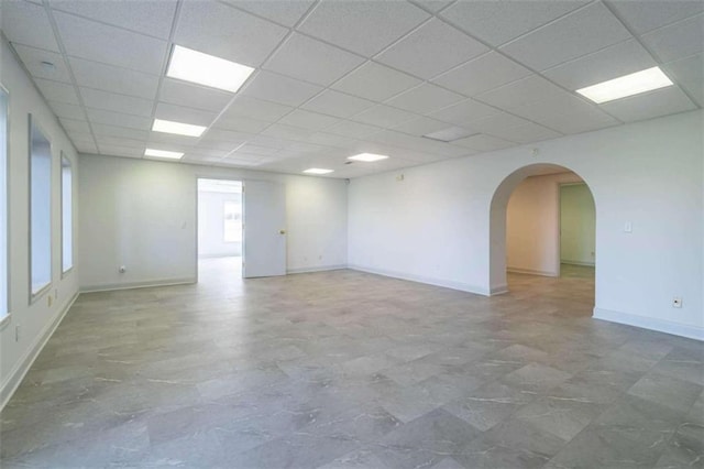 empty room featuring arched walkways, baseboards, and a paneled ceiling