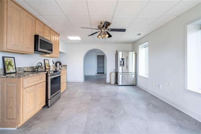 kitchen with a ceiling fan, a drop ceiling, arched walkways, baseboards, and stainless steel appliances