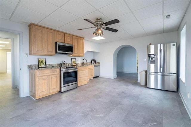 kitchen featuring a ceiling fan, light stone countertops, baseboards, arched walkways, and stainless steel appliances