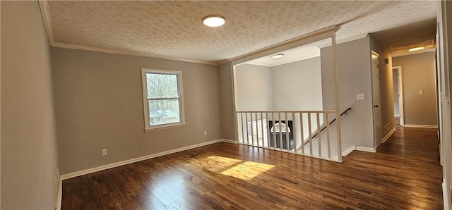 unfurnished room featuring baseboards, a textured ceiling, ornamental molding, and wood finished floors