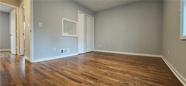 unfurnished room featuring dark wood-type flooring, visible vents, and baseboards