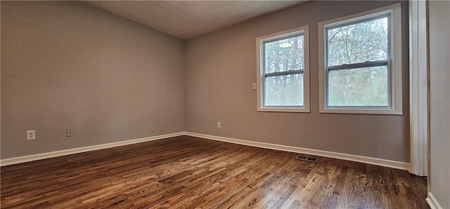 unfurnished room with dark wood finished floors, visible vents, and baseboards