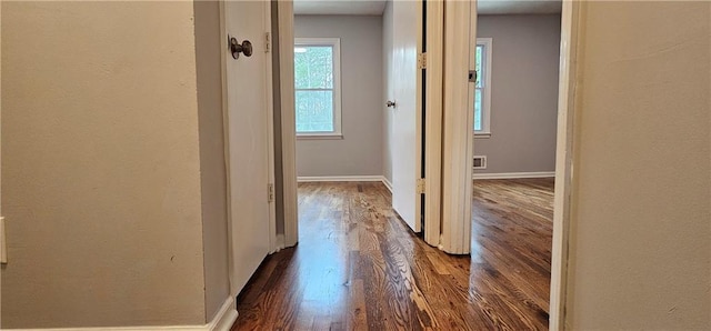 hall featuring dark wood-type flooring, visible vents, and baseboards