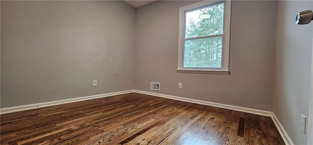 unfurnished room with dark wood-style floors, visible vents, and baseboards