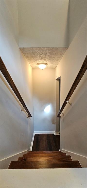 staircase featuring a textured ceiling, wood finished floors, and baseboards