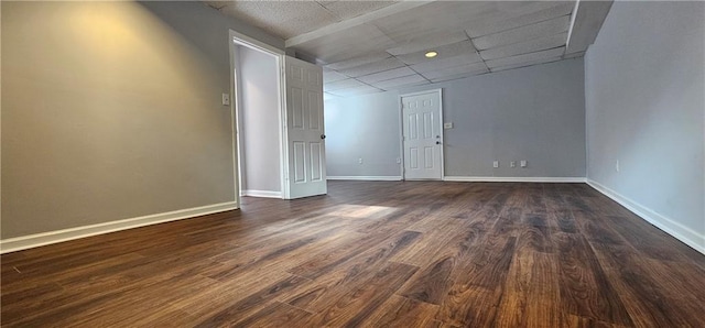 spare room featuring dark wood-style floors, a paneled ceiling, and baseboards