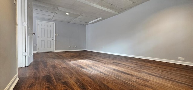 unfurnished room with dark wood-style flooring, a drop ceiling, and baseboards