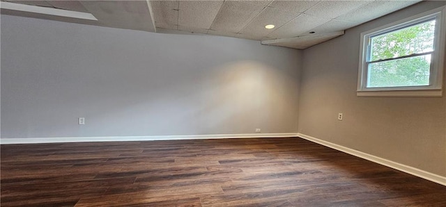 unfurnished room with dark wood-style flooring, a drop ceiling, and baseboards