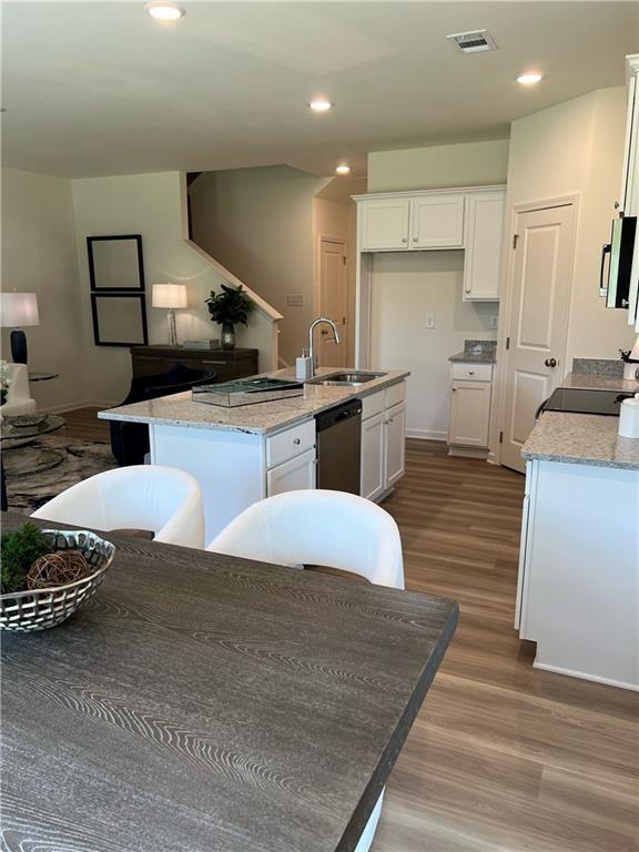 1567 Aiden Way Unit 34, Conyers, GA 30013 - kitchen featuring a sink, appliances with stainless steel finishes, a center island with sink, wood finished floors, and white cabinetry
