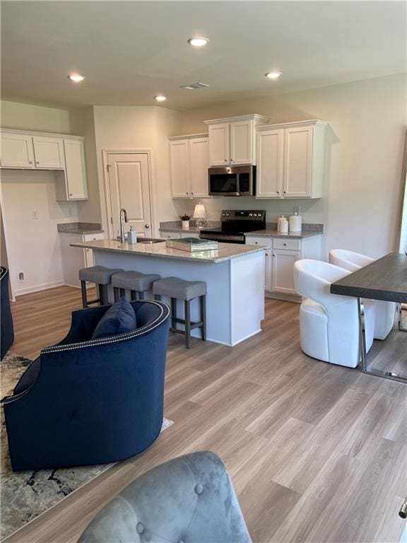 1567 Aiden Way Unit 34, Conyers, GA 30013 - kitchen with stainless steel appliances, white cabinetry, a center island with sink, light wood-style floors, and a sink