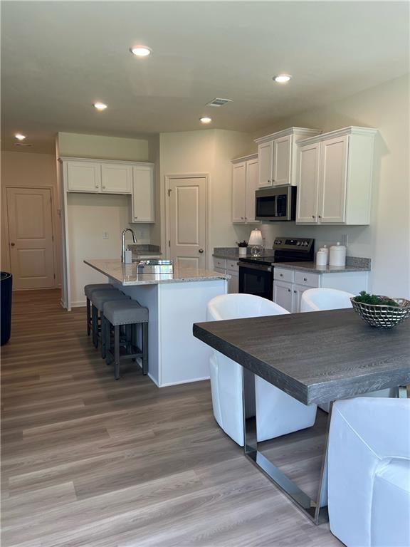 1567 Aiden Way Unit 34, Conyers, GA 30013 - kitchen featuring range with electric stovetop, stainless steel microwave, white cabinets, a breakfast bar, and a center island with sink