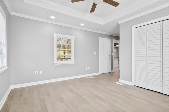 unfurnished bedroom with crown molding, light hardwood / wood-style flooring, ceiling fan, a tray ceiling, and a closet