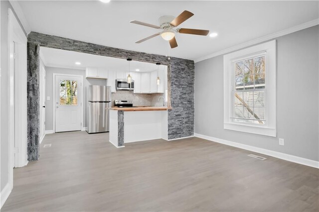 unfurnished living room featuring ceiling fan, crown molding, sink, and light wood-type flooring