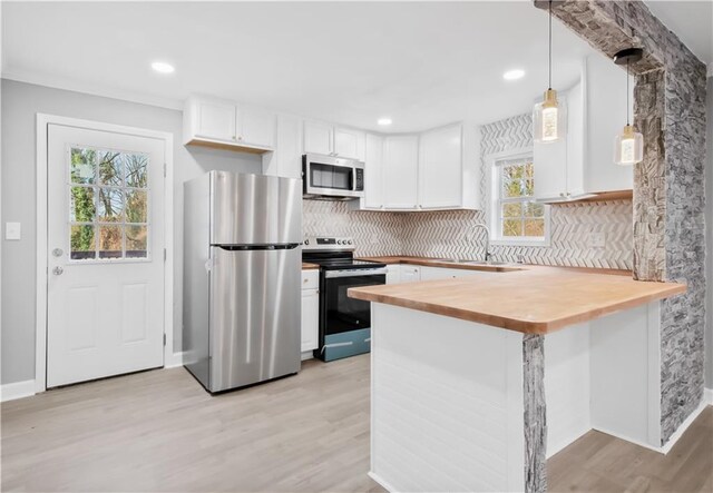 kitchen featuring kitchen peninsula, appliances with stainless steel finishes, a wealth of natural light, white cabinetry, and hanging light fixtures