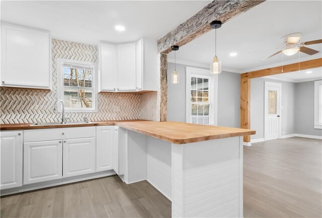 kitchen with pendant lighting, white cabinetry, butcher block counters, and sink