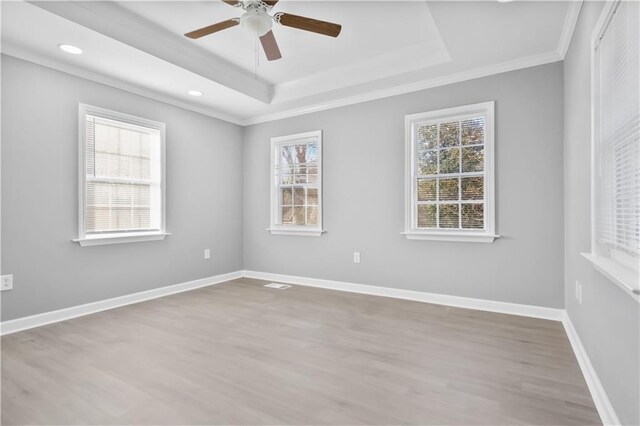 empty room with a healthy amount of sunlight, a raised ceiling, light hardwood / wood-style floors, and ornamental molding