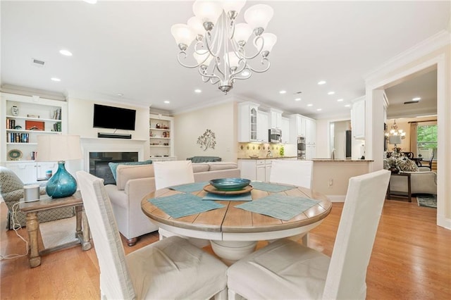 dining space featuring a chandelier, light wood-style flooring, a glass covered fireplace, ornamental molding, and recessed lighting