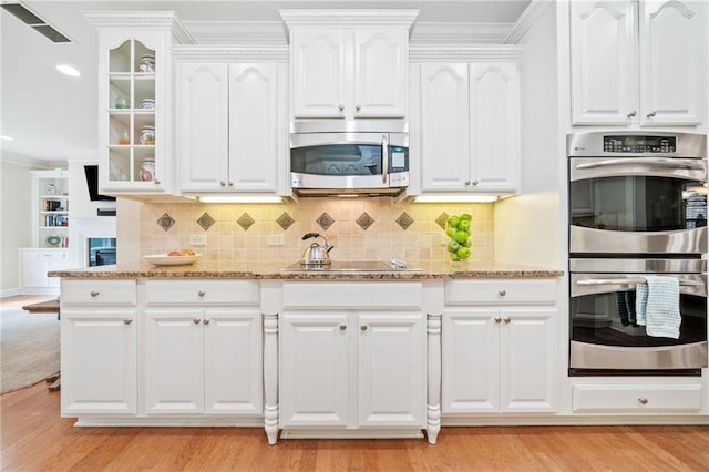kitchen featuring appliances with stainless steel finishes, light stone countertops, glass insert cabinets, ornamental molding, and decorative backsplash