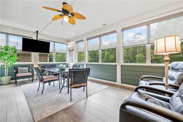 sunroom / solarium featuring a wooden deck, a ceiling fan, outdoor dining area, and wood finished floors