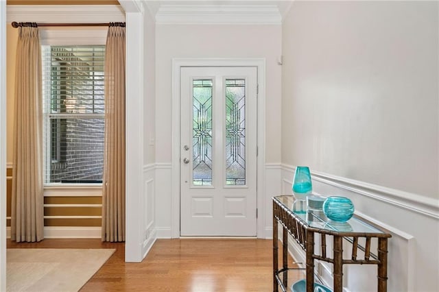 entryway featuring wood finished floors, ornamental molding, wainscoting, and a decorative wall